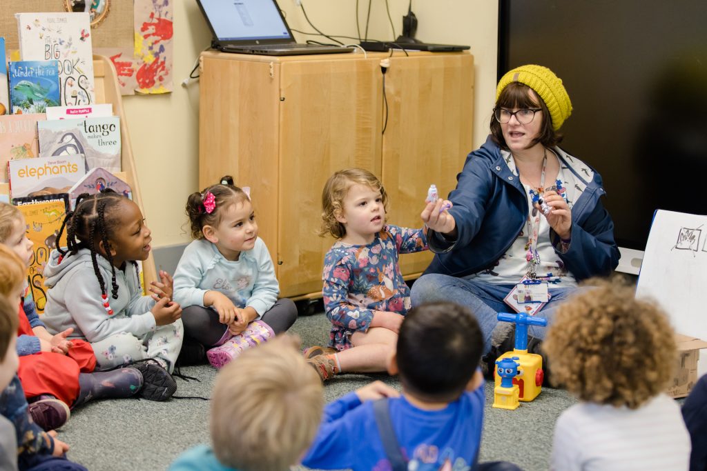 Photograph of a nursery leader showing a small bottle to a group of nursery children