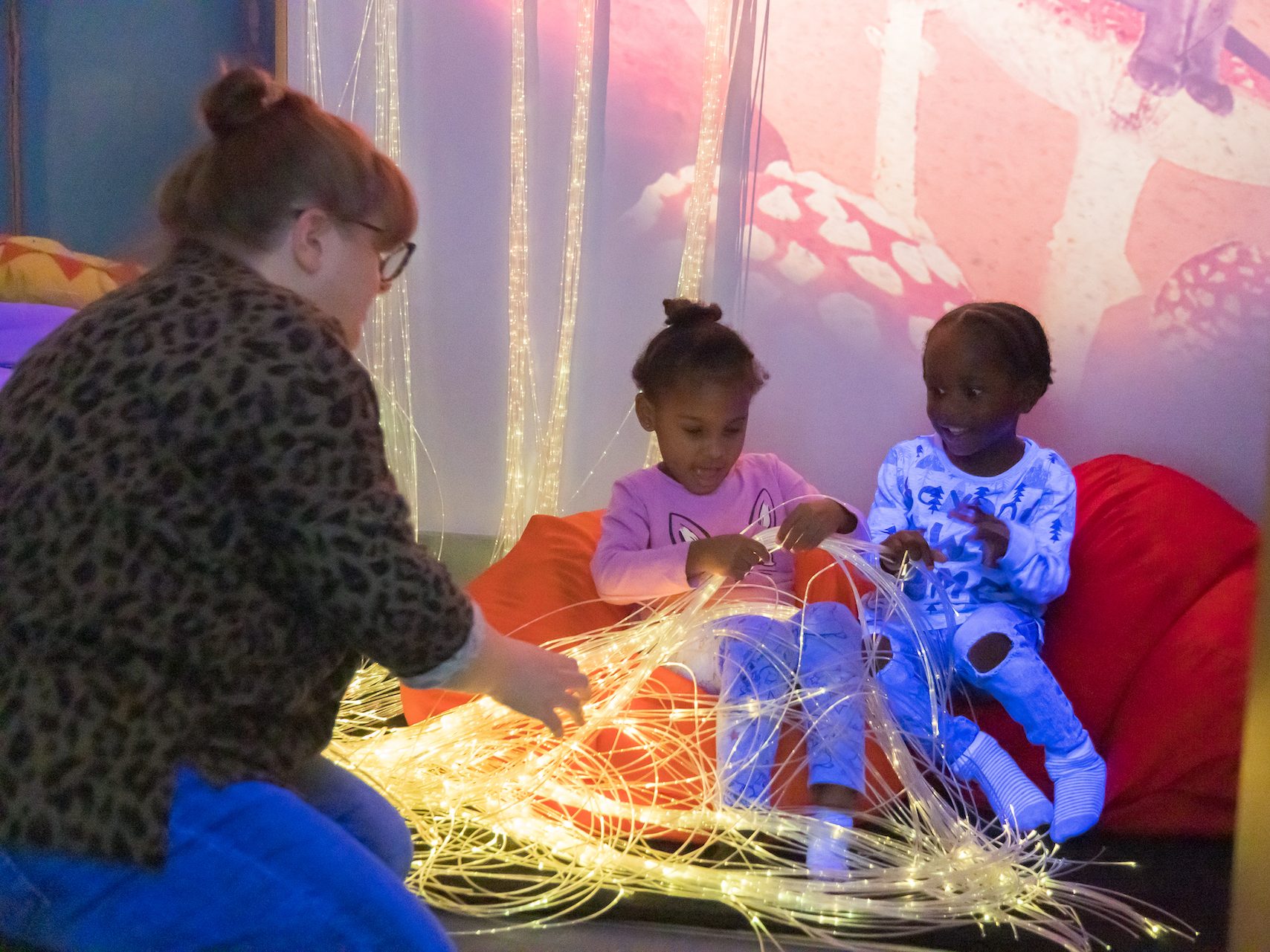 Two nursery children exploring lights in the sensory room, supported by their teacher