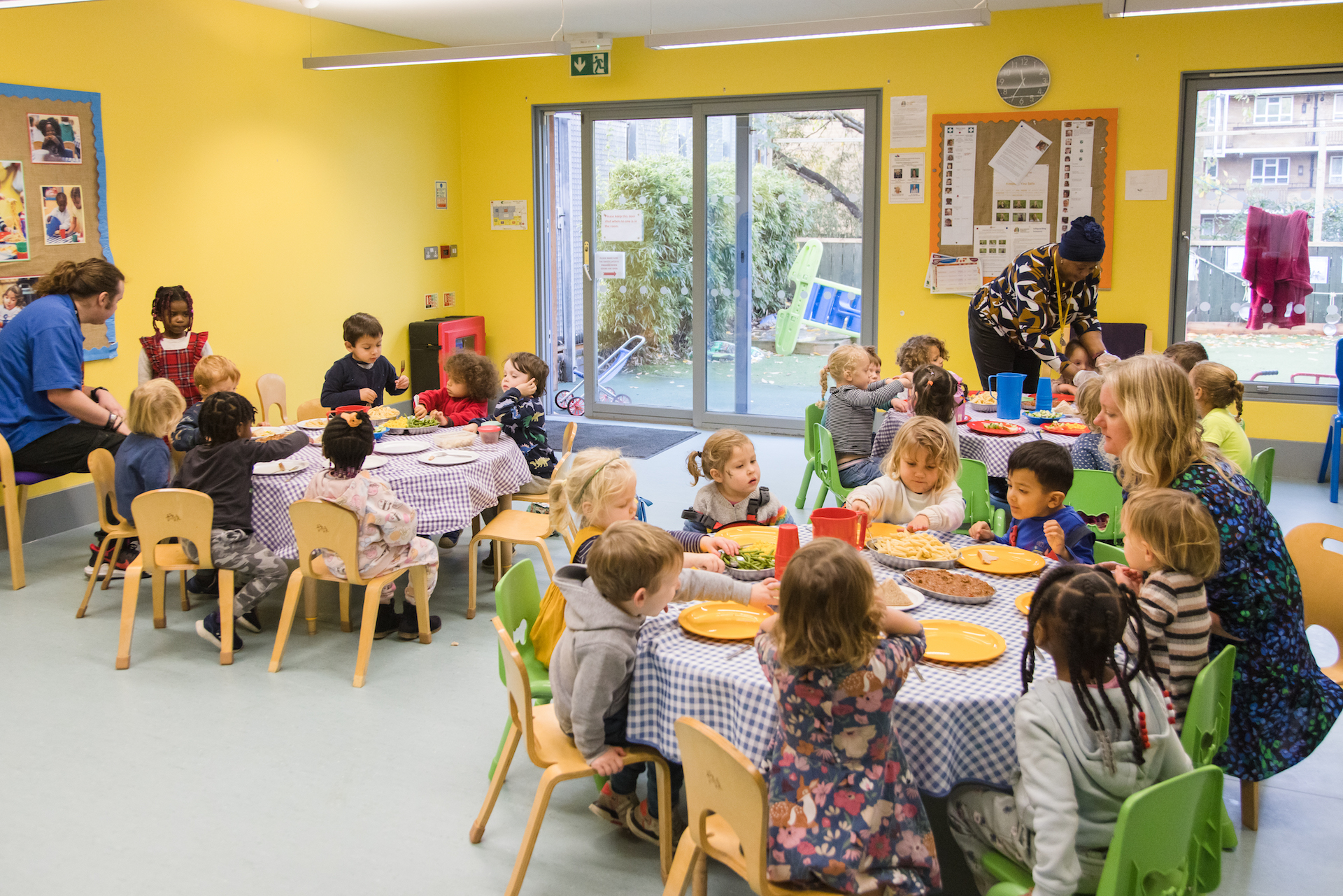 Children enjoy lunch together at tables in a bright room with large windows